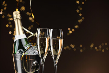 Champagne in glasses and ice bucket with bottle on brown background with blurred lights, space for text