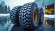 © Iurii - Three rugged truck tires set on asphalt with blurred warehouse backdrop