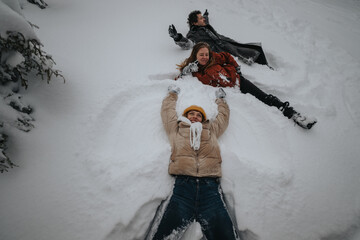 Poster - Group of friends spending time outdoors during snowy weather, lying on the ground making snow angels, and enjoying a joyful and playful winter activity together, embracing the spirit of friendship and