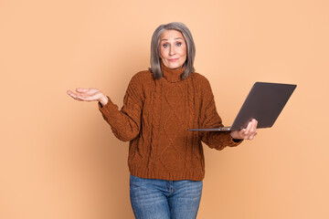 Wall Mural - Mature woman with a laptop showing a confused expression on a beige background