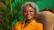 © Phatharaporn - Smiling woman with short gray hair wearing round glasses and a mustard yellow shirt sits in an antique chair against a lush green backdrop.
