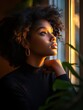 © Lisouski Uladzimir - A black woman gazing out of a window bathed in warm golden sunlight