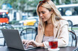 © nenetus - Beautiful young woman working with her laptop while drinking red tea in a coffee shop terrace.
