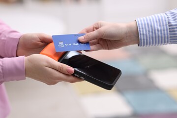 Wall Mural - Woman paying with credit card via terminal against blurred background, closeup