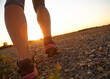 © peopleimages.com - Person, feet and shoes with dirt road for fitness, running or outdoor exercise on mountain sunset. Closeup, athlete or runner with sneakers on gravel street for cardio, training or workout in nature