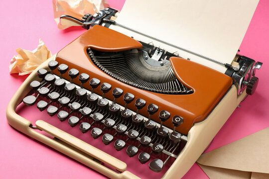 Vintage typewriter, crumpled paper and envelope on pink background, closeup