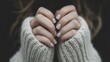 © musa - Close-up of woman's hands with soft, white manicure, clasped together inside a cozy cream-colored knitted sweater.