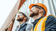 © mandm. - Supply Chain Security Risks and Vulnerabilities. Two construction workers in helmets and safety gear looking up with a container in the background.