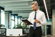 © ty - Businessman walking in office corridor with documents and takeaway coffee