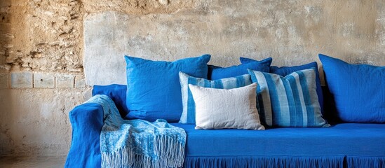 Poster - Cozy blue sofa adorned with vibrant pillows and blankets against rustic wall perfect for interior decor inspiration and text placement