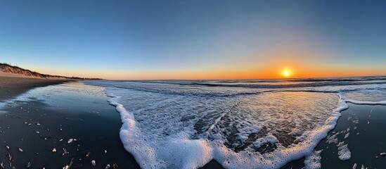 Poster - Serene sunset illuminating the wavy shoreline with foam on the sand and a vast blue sky offering ample blank space for text and design.