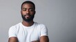 © AbstractAI - Confident young African American man in a white t-shirt standing against a neutral gray background with arms crossed and a thoughtful expression