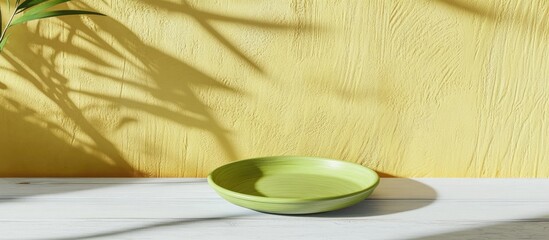 Poster - Green ceramic plate on white wooden table with yellow textured wall and shadows of plants in background Copy Space
