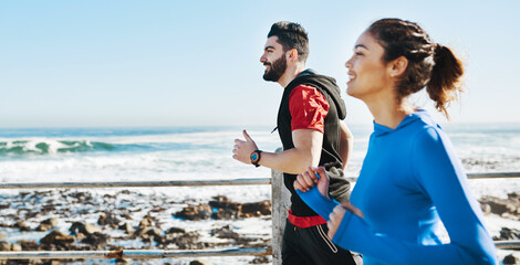 Couple, fitness and running with smile by beach for cardio workout, exercise or training together on promenade. Active people, wellness or happy runners in race, sprint or jog by sea or ocean coast