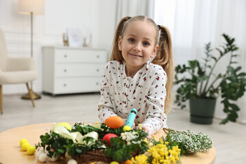 Little girl with hot glue gun creating Easter composition at table indoors