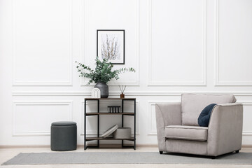 Poster - Console table with decor and armchair near white wall in room. Interior design
