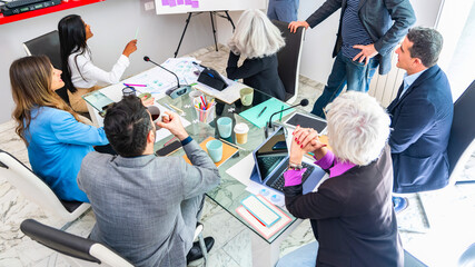 multiracial team of diverse partners mature business man and business woman discussing project at office table – multicultural professional businesspeople working together in boardroom 