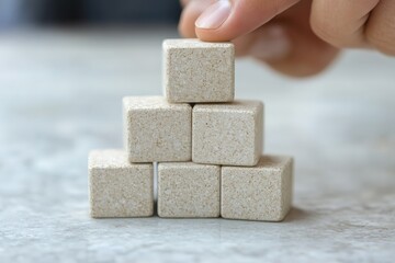 Poster - Hand carefully places a cube on top of a small pyramid of cubes on a marble surface