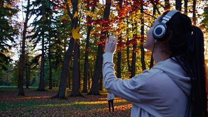 Poster - An atmospheric view of a secluded forest clearing, a person in headphones bathed in the warm glow of the setting sun, autumn leaves swirling around.