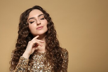 Canvas Print - Beautiful young woman with long curly brown hair in golden sequin dress on beige background, space for text