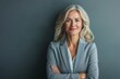 © Hunman - Elegant middle-aged woman wearing a blazer and smiling warmly, hands clasped in front, over a neutral gray background.