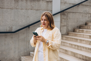 Wall Mural - Happy young woman with mobile standing on steps in city. Holidays, technology and tourism concept. Female tourist searching direction on smart phone while traveling abroad in summer