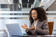 © Tetiana - Smiling young African American woman in suit and headset sitting at desk in office and gesturing with hands talking on video call on laptop