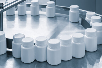 Poster - Row of white plastic containers with lids for medicines or vitamins or active dietary supplements on conveyor belt of pharmaceutical factory