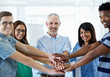 © Anne B/peopleimages.com - Happy people, portrait and creative team with hands together for motivation, collaboration or support at office. Group, employees or piling with smile for meeting, huddle or unity in solidarity