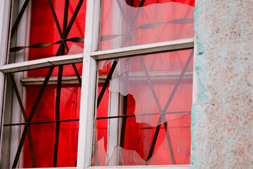 Aufkleber - A window with a broken glass pane and a red curtain hanging in front of it.