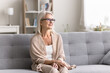 © fizkes - Positive pensive mature female retiree in eyewear sit on comfy sofa at living room look away with smile. Happy senior lady lost in pleasant memories thoughts relax at cozy home enjoy silence serenity