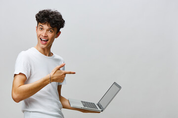 Wall Mural - Happy young man pointing at laptop on a plain light background, showcasing excitement and positivity while promoting technology and creativity in a modern digital workspace