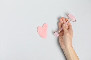 Wall Mural - Woman with face roller and gua sha tool on light background, top view. Space for text