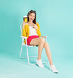 © sitthiphong - Happy smiling young Asian woman sit in deckchair hold thai passport and credit card in blue background. Tourist travel trip journey concept