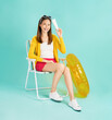 © sitthiphong - Happy smiling young Asian woman sit in deckchair and holding white unbranded cosmetics tube mockup in blue background.