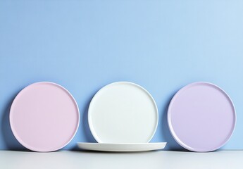 Wall Mural - Three pastel colored plates arranged on a white surface against a textured light blue background. The plates are light purple, white, and lavender