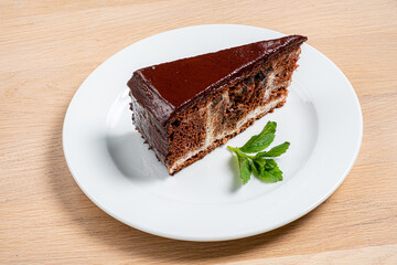 Wall Mural - A decadent slice of chocolate cake sits elegantly on a white plate, featuring rich chocolate frosting and a pop of fresh mint, ideal for dessert enthusiasts who crave indulgence. 