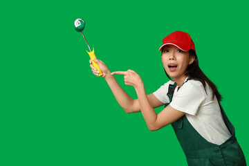 Wall Mural - female asian shocked painter pointing at roller on green background