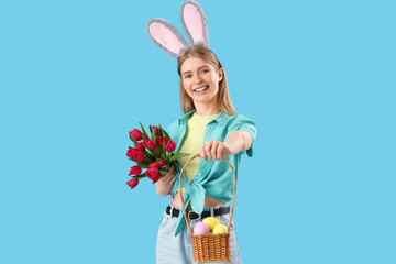 Wall Mural - Young woman in bunny ears with tulips and Easter eggs on blue background