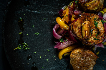 Wall Mural - Slice of roasted pork tenderloin with vegetables, pink onion and yellow pepper on a black plate on a dark background. Beautiful, restaurant presentation of the dish. Copy space.