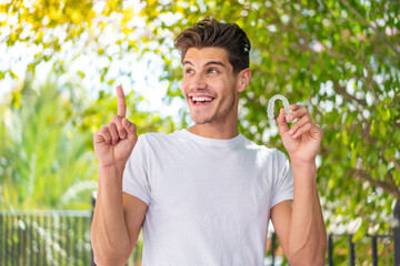 Young caucasian man holding invisible braces at outdoors intending to realizes the solution while lifting a finger up