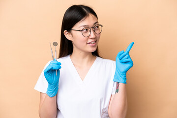 Wall Mural - Dentist Chinese woman holding tools isolated on beige background pointing up a great idea