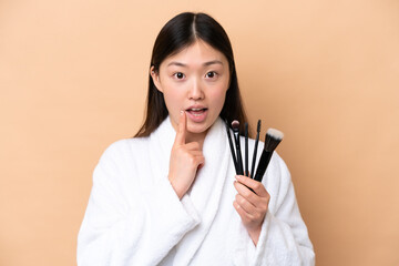 Wall Mural - Young Chinese woman isolated on beige background holding makeup brush