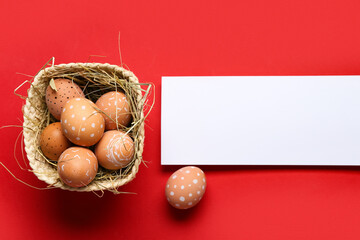 Wall Mural - Basket with Easter eggs and blank card on red background. Top view