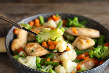 Wall Mural - Frying pan with tasty chicken fillet and vegetables on wooden table, closeup