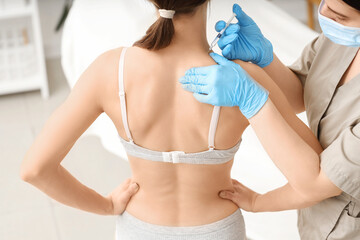 Young woman receiving injection at cosmetologist's office, back view