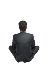 Poster - Rear view of a man in a formal dark suit sitting cross-legged, isolated on a clean white background. Concept of professionalism and contemplation