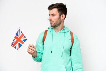 Wall Mural - Young student caucasian man holding an United Kingdom flag isolated on white background looking to the side and smiling