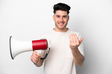 Young caucasian man isolated on white background holding a megaphone and inviting to come with hand