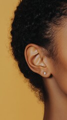 Poster - Close up of a woman's ear with a small diamond earring, highlighting the concept of hearing, sound, and audiology against a vibrant yellow backdrop